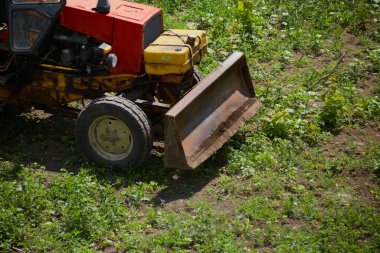 Bir kazıcının ön tarafı uzun yeşil çimenleri temizler, bir inşaat alanı hazırlar, eski bir traktör yeşil çimenleri, alan temizliğini, işin başlangıcını, doğayı ve makineleri temizler.