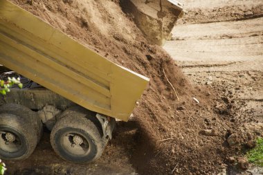 Kamyonun yatağı yükseliyor, toprağın düşmesine izin veriyor, yakın plan çekimde vurgulanıyor.