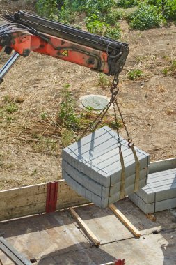 Yükleyici vinç kamyon yatağından beton bahçe bariyerlerini indiriyor, kaldırım taşlarıyla inşaat işi yapıyor, kaldırım çitleriyle dolu bir uçuşu boşaltıyor.