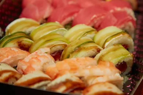 Filedelfiya suşisi avokado ve somon ile birlikte koyu renkli kutuda ve ılık ışıkta bulanık arka planda, yumuşak ılık ışıkta bulanık suşi, içeriğinin dokusunu ve detaylarını gösteriyor..