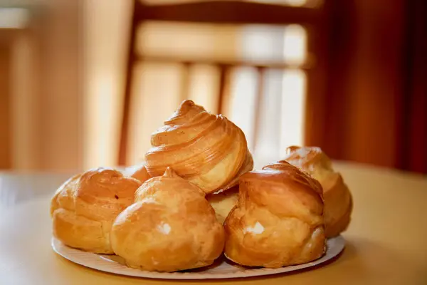 Kafedeki bir masada profiterol tabakası, arka planda hafif bir çekim, yakın çekim pişirme dokusu, yakın çekim kremalı hamur işleri. 