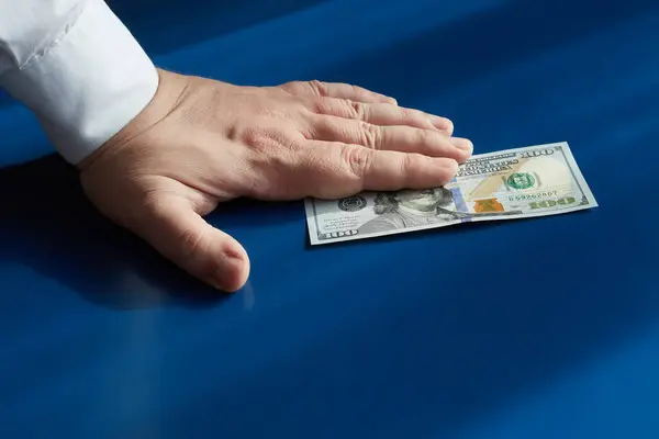 Bir el, gün ışığında mavi bir arkaplanda yüz dolarlık banknot tutar.