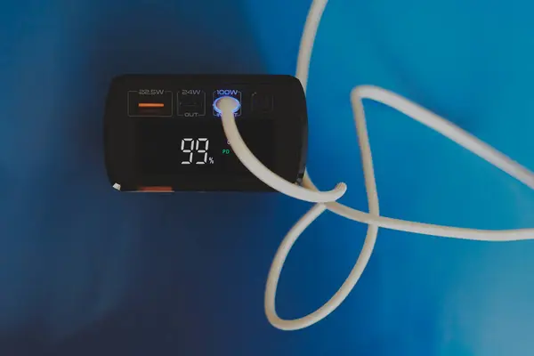 Bağlı beyaz kabloyla bir güç bankasının yakın çekimi ve ekrandaki rakamlar yüzde 99, pil şarj seviyesi, taşınabilir powe