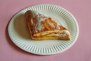 Pembe arka planda tek kullanımlık tabağa şeker serpiştirilmiş poğaça üçgeni. Pembe arka planda tek kullanımlık beyaz bir tabağa şeker serpiştirilmiş turta, abur cubur, fast food, bir turta..