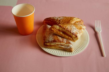 Tek kullanımlık bir tabağa şeker serpiştirilmiş üçgen puf böreği, tek kullanımlık çatal, pembe arka planda tek kullanımlık bardak, fast food, sokak yemeği..