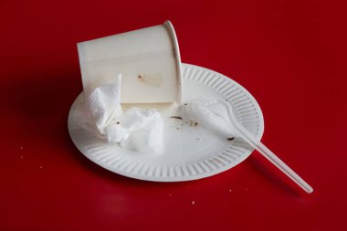 Kırmızı arka planda kullanılmış peçete ve tek kullanımlık çatal ve kağıt bardakla tek kullanımlık tabak, ev yapımı, partinin sonu.