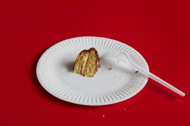 Küçük bir parça çikolatalı pasta ve tek kullanımlık çatal kırmızı arka planda beyaz bir tek kullanımlık tabağın üzerine uzanmış, kendi payına düşen pasta, sıkı bir diyet rejimi