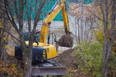 Kazı kovası toprağı toplar ve taşır, sonbahar mevsiminde ormanlık alanda kazı yapar, yeni bir inşaat alanında çalışır..