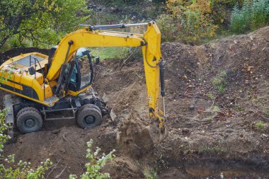 Kazıcı kovayla çukur kazıyor, kazıcı kovayla toprağı kazıyor, kazıcı kovayla inşaat alanında çalışıyor.