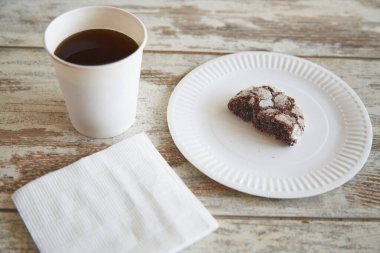 Eski bir ahşap masa üzerinde çatlaklar olan çikolatalı kurabiyenin yarısını içeren bir kağıt tabak.