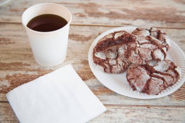 Bir bardak kahve ve kağıt peçeteyle eski ahşap bir masanın üzerinde çatlaklar olan bir tabak çikolatalı kurabiye. Yakın plan, ev yapımı..