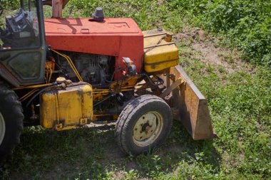 Eski bir traktör, araziyi bir inşaat projesi için hazırlayan kovayla uzun otlardan bir tarlayı temizliyor. Kırsal kesimi inşa, mühendislik ve dönüştürme konsepti.