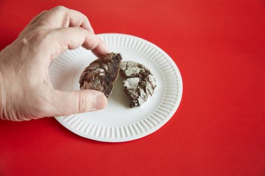 Kırık bir çikolatalı kurabiyeyi kırmızı arka plan, yakın plan, ev yapımı, çikolatalı kurabiyeler, tabağın üzerindeki kırıntılarla alan bir el.. 