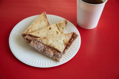 Kırmızı arka planda şeker ve tarçınlı taze fırınlanmış tortilla cipsi, bir bardak kahvenin yanında.