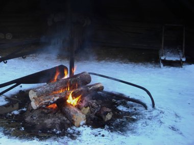 Kış aylarında kardaki büyük odunlardan yapılmış bir kamp ateşi, kırsal alanda kar üzerinde bir ateş, kış arka planında güçlü yumuşak bir odak.