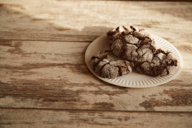 Tahta bir masa üzerindeki çatallı çikolatalı kurabiyelerle dolu beyaz bir tabak. Güneş ışığı demeti, sade atmosfer, tatlı pişirme..