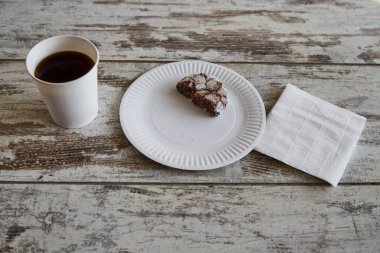 Eski bir ahşap masa üzerinde çatlak olan yarım çikolatalı kurabiye ve beyaz kağıt peçetelerin yanında bir fincan kahve, yakın plan, yarım porsiyon diyet.