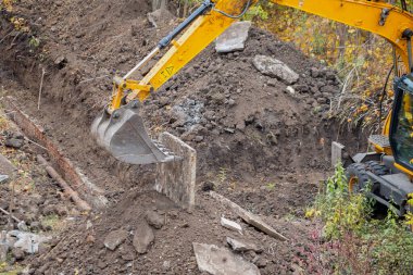 The excavator bucket moves a concrete slab fragment, cleaning bulky construction debris, the excavator bucket lifts a concrete slab during repair work.