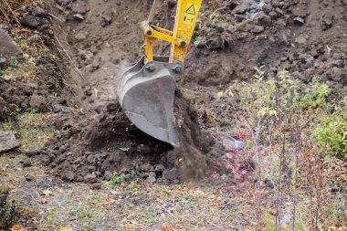 Close-up of an excavator bucket dumping soil against the background of a dug trench, new construction, construction industry and environmental protection.