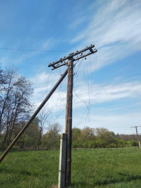 Eski, terk edilmiş, yarı mahvolmuş zaman elektrik direği mavi gökyüzüne karşı bir tarlada kopmuş kablolar. Görsel projelerinizdeki terk edilme atmosferini ve zamanı aktarmak için.
