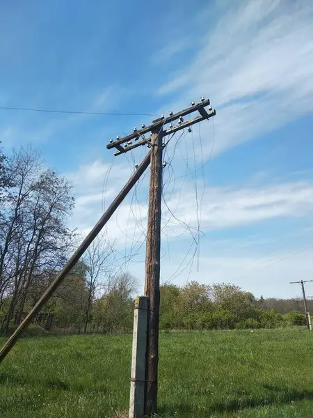 Eski, terk edilmiş, yarı mahvolmuş zaman elektrik direği mavi gökyüzüne karşı bir tarlada kopmuş kablolar. Görsel projelerinizdeki terk edilme atmosferini ve zamanı aktarmak için.