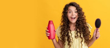 Şok olmuş kıvırcık saçlı çocuk tarak ve şampuan şişesini tutuyor. Gençlerin saç stili. Çocuk saç bakımı, yatay poster. Kopyalama alanı olan başlık