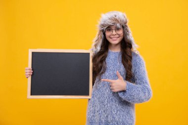 Kara tahtalı, kışlık şapkalı küçük bir kız. Liseli kız fotokopi odası ve okul satışı için karatahta tutuyor. Mutlu kız yüzü, pozitif ve gülümseyen duygular