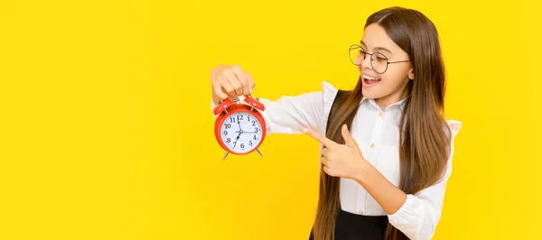 surprised kid in school uniform and glasses point finger on alarm clock showing time, shopping time. Teenager child with clock alarm, horizontal poster. Banner header, copy space