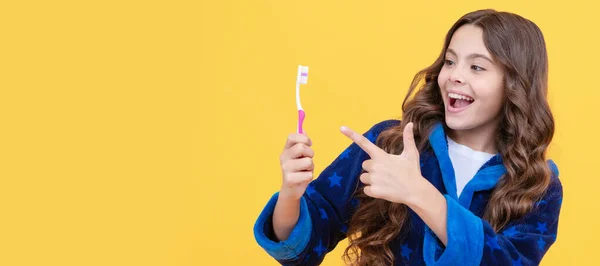 happy child girl in cozy bathrobe pointing finger on toothbrush in morning, dental care. Banner of child girl with teeth brush, studio portrait, header with copy space