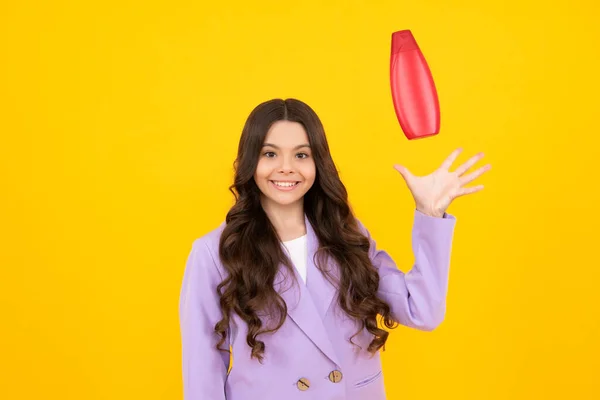 Teenager child girl showing bottle shampoo conditioners or shower gel isolated on yellow background. Hair cosmetic product. Mock up bottle. Happy teenager, smiling emotions of teen girl
