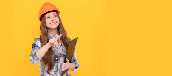 Builder teenager girl in helmet. happy teen girl in helmet and checkered shirt making notes on clipboard, busy. Child in hard hat horizontal poster design. Banner header, copy space