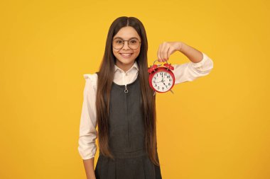 Mutlu kız yüzü, pozitif ve gülümseyen genç kız sarı arka planda saati tutuyor. Sabahın erken saatleri, günlük program. Çocuk kontrol zamanı. Geç kalmayın. Alarmı olan dakik bir çocuk. Son teslim tarihi