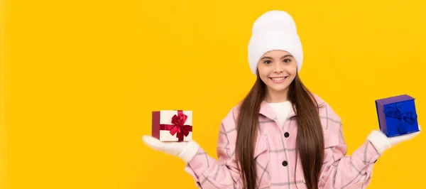 戴着帽子和手套的快乐的孩子选择黄色背景的礼物盒 做出选择 圣诞小女孩的横幅 带复制空间的工作室小孩冬季肖像 — 图库照片