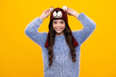 Beautiful winter kids portrait. Teenager girl posing with winter sweater and knit hat on yellow background. Happy teenager, positive and smiling emotions of teen girl