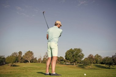 Profesyonel golf sahasında erkek golfçü. Golf sopasıyla şapkalı golfçünün portresi. İnsanların yaşam tarzı. Adam mavi gökyüzüyle yeşil çimlerde oyun oynuyor. Yaz etkinliği. Profesyonel spor..