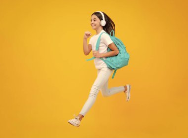 Happy teenager portrait. School girl in headphones on isolated studio background. School and music concept. Jump and run, jumping child