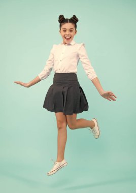 Happy funny excited jumping teenager. Happy schoolgirl, positive and smiling emotions of teen girl. Full length jump of teenager girl on blue isolated studio wear casual skirt and shirt