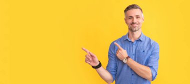 Gülümseyen yetişkin bir adam kol saati ile sarı arka planda işaret parmağı, kopyalama alanı, buluşma dakikaları. İnsan yüzü portresi, kopyalama alanı olan pankart