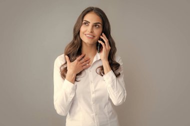 Gri arka planda izole edilmiş, cep telefonuyla konuşan gülümseyen bir kadın. Cep telefonu olan kız
