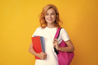 Sırt çantalı hoş bir öğrenci kadın, sarı arka planda bazı belgeler ve kitaplar tutuyor. Sırt çantasındaki gülümseyen genç kız öğrencinin portresi. Not defterleri. Lise üniversitesinde eğitim