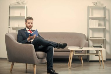 Takım elbiseli, düşünceli, olgun iş adamı ofiste oturup kitap okuyor..