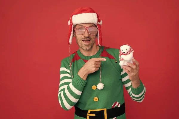 パーティーの眼鏡の男が赤い背景のクリスマスの飾りの雪だるまに指を向けた 新年明けましておめでとう メリー クリスマス セルフコスチュームとサンタクラスの帽子の男 — ストック写真