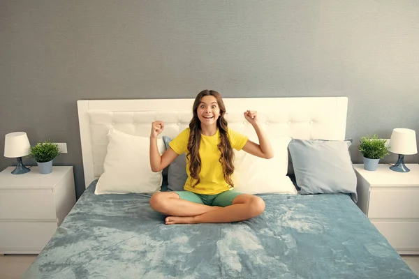 Expressive emotional excited teen girl. Teenager child in bed. Kid relaxing in bedroom interior