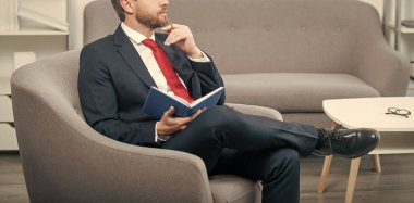 Takım elbiseli olgun bir işadamı okuma odasında oturup not defterine not alır..