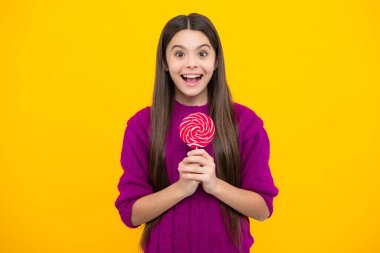 Funny child with lollipop over yellow isolated background. Sweet childhood life. Teen girl with yummy caramel lollipop, candy shop. Teenager with sweet sucker