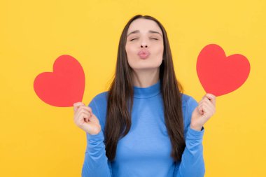 Aşkı hisseden bir kız. Sarı arka planda elinde kağıt kalple gülümseyen güzel bir kadının portresi. Aşk konsepti