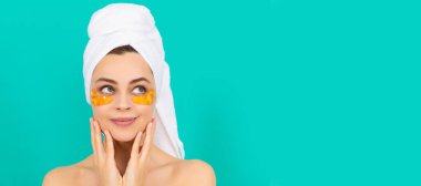 Güzel yüzlü kadın, yüz portresi. Gülümseyen genç kadının yüzünde havluyla kolajen altın göz bantları var. Güzel kadın, izole edilmiş yüz portresi, taklit alanı olan pankart.