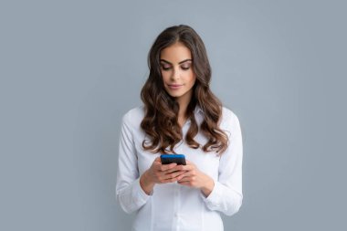 Akıllı telefonu olan ciddi bir kadın. Cep telefonu olan genç bir kadın. Gri arka planda akıllı telefonu olan bir iş kadını