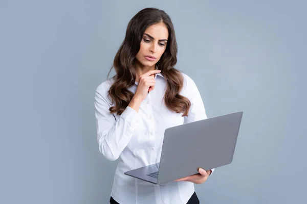 在灰色背景下使用笔记本电脑的愤怒而悲伤的商业女性 — 图库照片