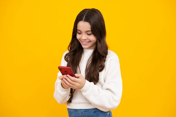 少女使用智能手机 分享社交媒体 用手机聊天时穿着时髦的休闲装 与黄色背景隔离 带着智能手机的孩子快乐的脸 微笑的女孩 — 图库照片
